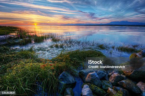 Relaxing Summer River Sunset With Green Grass And Distant Mountains Stock Photo - Download Image Now