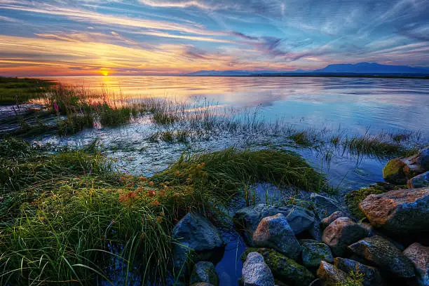 Photo of Relaxing summer river sunset with green grass and distant mountains