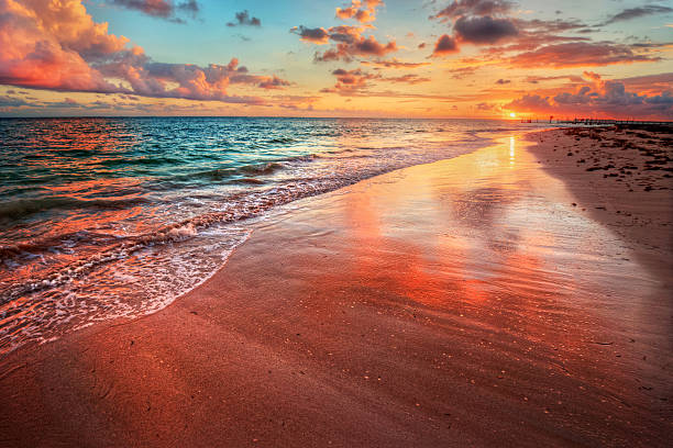 incrivelmente colorido pôr-do-sol na praia do mar, com areia vermelha refletivos - marquesas islands - fotografias e filmes do acervo