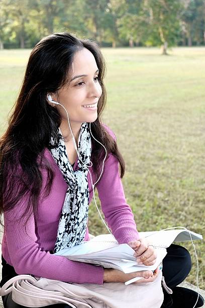 istock Indian female student listening music on grass. 535372037