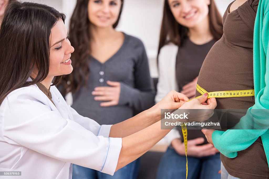 Pregnant women Cheerful young female doctor is measuring belly of young pregnant woman. 2015 Stock Photo