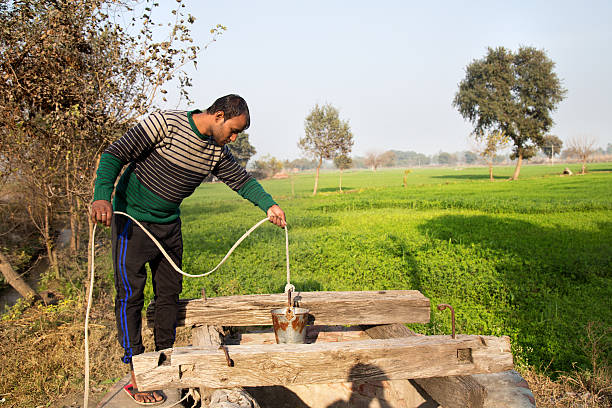 Men Collecting Water From Deep Well Situated in Rural India near Green Field.