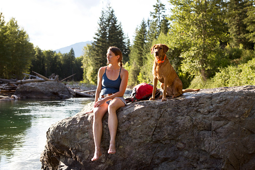 A hiker and her dog sitting by a river.