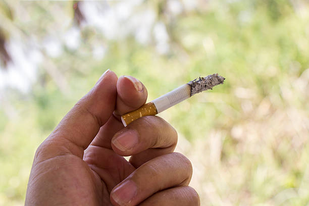 mano e una sigaretta su uno sfondo in legno. concetto di dipendenza - indiscreet foto e immagini stock