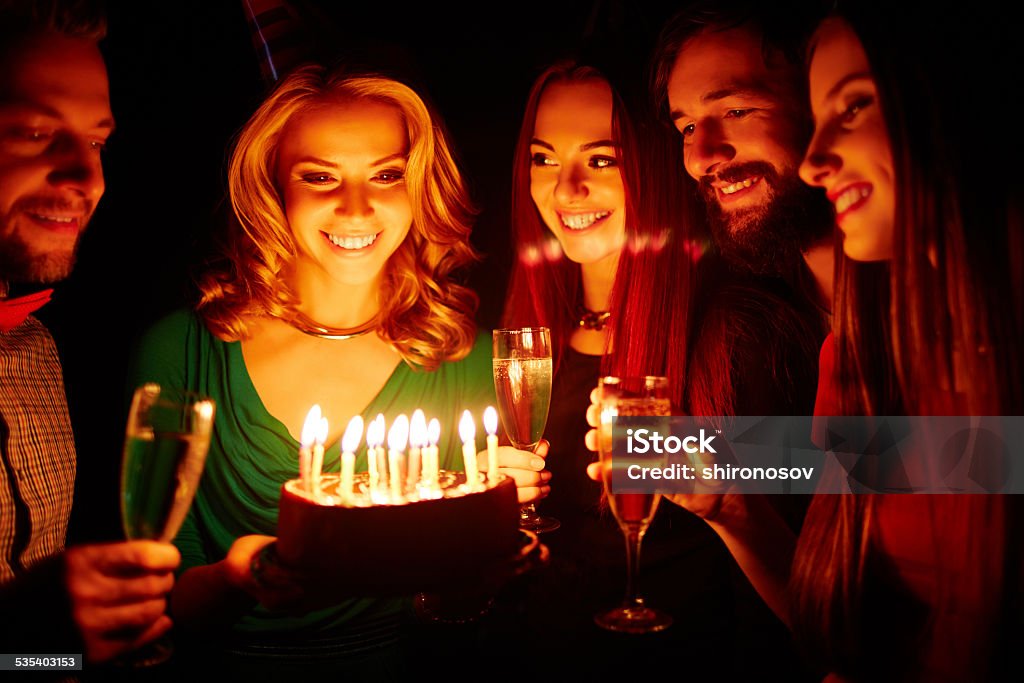 Birthday wonder Pretty girl holding birthday cake with burning candles, her friends with champagne surrounding her 2015 Stock Photo