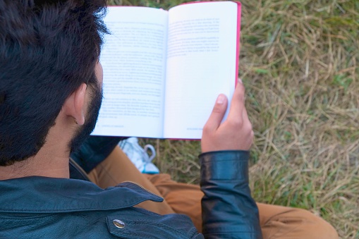 male college student reading over grass