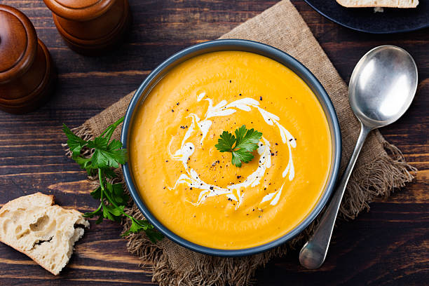 Pumpkin and carrot soup with cream and parsley Pumpkin and carrot soup with cream and parsley on dark wooden background Top view pumpkin soup photos stock pictures, royalty-free photos & images