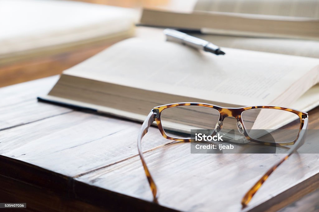 Education concept. Glasses on opening book in library or cafe. Eyeglasses Stock Photo