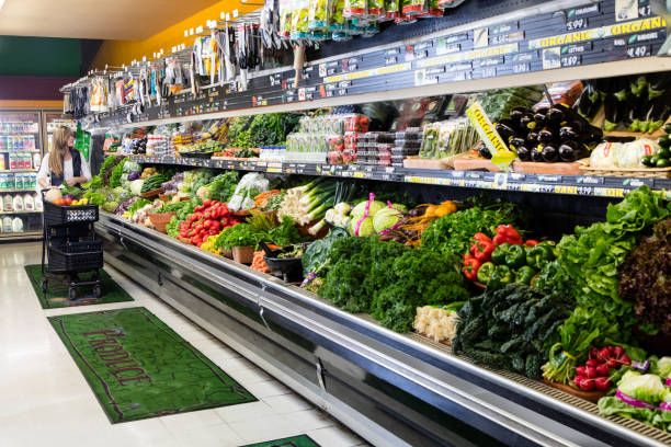 Woman Grocery Shopping Woman with cart shopping in grocery store in the produce section. produce section stock pictures, royalty-free photos & images