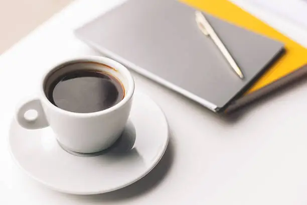 Close up of cup of coffee near notebooks on table