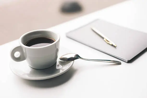 Close up of mug of coffee with writing-pad on desk