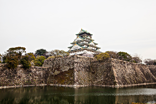 Osaka, Japan - April 4, 2013: The iconic five storey tower of Osaka Castle surrounded by the steep stone walls and tranquil moat of Osaka Castle Park in the heart of downtown Osaka, Japan's vibrant second city. 