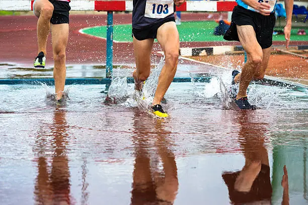 Group of male athletes at 3000 metres steeplechase, water jump