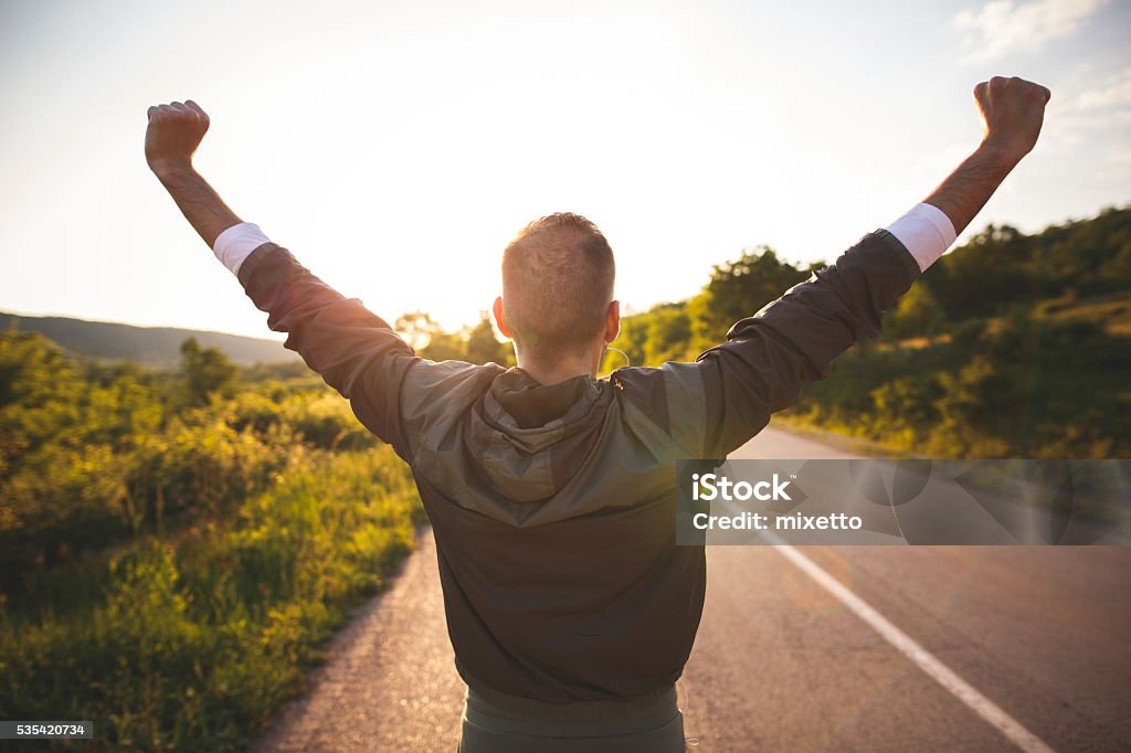 Man raising arms Sport and life achievements and success concept. Sporty man raising arms towards beautiful sunset on the road Men Stock Photo