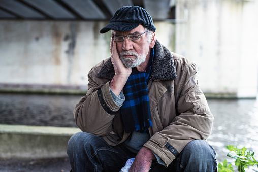 Depressed homeless man sitting on concrete wall under bridge.