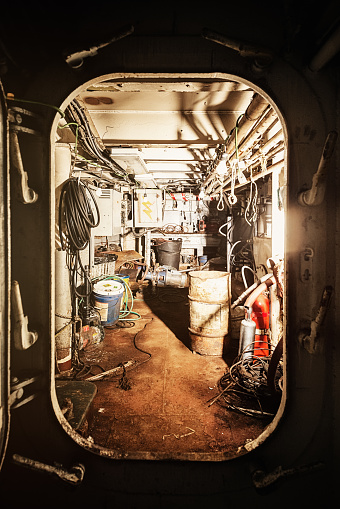 Light spills from the hatch door of a parts storage room in an abandoned tugboat.