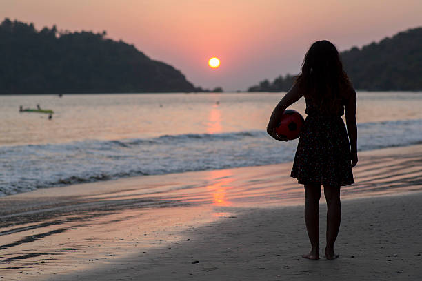 Girl_Silhouette_sunset A silhouette of a girl standing on the beach with a ball under her arm watching the sunset over the ocean in Goa, India palolem beach stock pictures, royalty-free photos & images