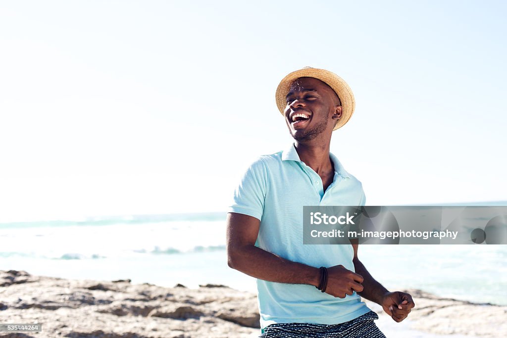 Cheerful young african man enjoying at the beach Portrait of cheerful young african man with hat enjoying at the beach on summer day Men Stock Photo