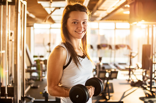 Young sporty woman lifting steel dumbbell in gym.