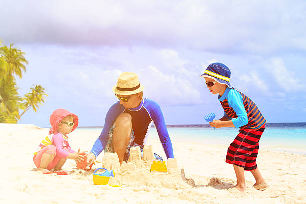istock father and two kids playing with sand on beach 535449072