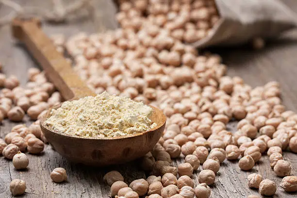 Chickpea flour in a wooden spoon, chickpeas on old wooden background