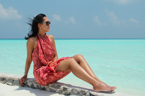 Tanned girl with dark hair in red pareo in the Maldivian beach