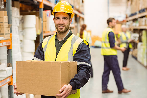 Warehouse worker smiling at camera carrying a box stock photo
