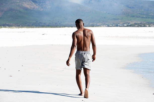 jeune homme marchant pieds nus sur la plage - shorts rear view summer beach photos et images de collection