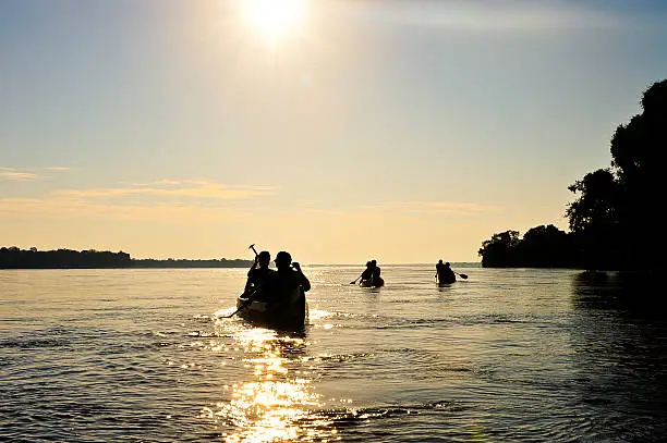 Silhouetted figures padding into the sun on the Zambezi River