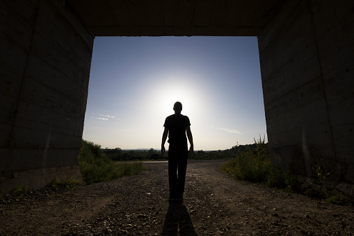 Man standing at large passage of concrete building, blocking sunlight at sunset. Rear view. Photo is taken with dslr camera and wide angle lens.