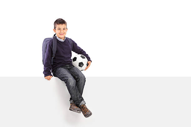 istock Schoolboy holding soccer ball seated on a panel 535464619