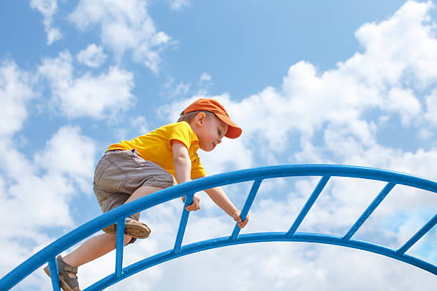 little boy climbs up the ladder on the playground child climbs confidently up the ladder against the blue sky. copy space for your text schoolyard stock pictures, royalty-free photos & images