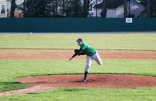Side view of a high school baseball pitcher pitching during a baseball game.