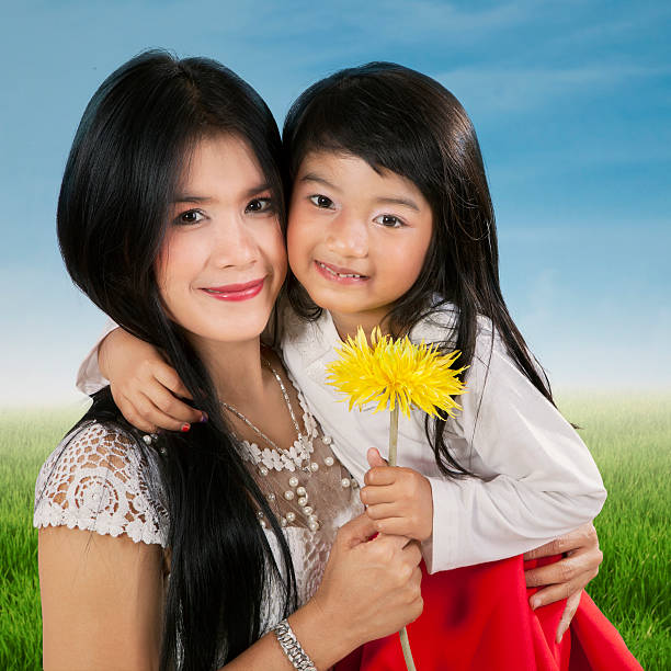 Portrait of happy child smiling at the camera while holding a flower with her mother