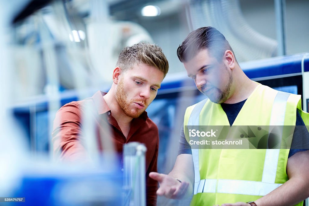 Young men working in manufacturing facility Young manager and foreman looking at machine on production line Engineer Stock Photo