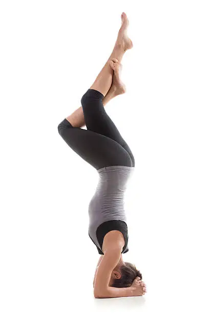 Sporty yoga girl on white background doing a handstand in pose shirshasana (Sirshasana) with entwined legs