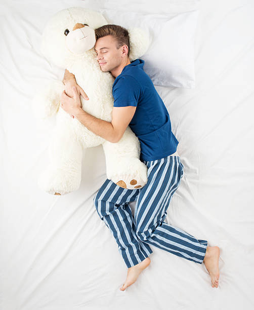 Man sleeping with large teddy bear Young man sleeping in an embrace with a large white teddy bear. Top view photo man with teddy bear stock pictures, royalty-free photos & images