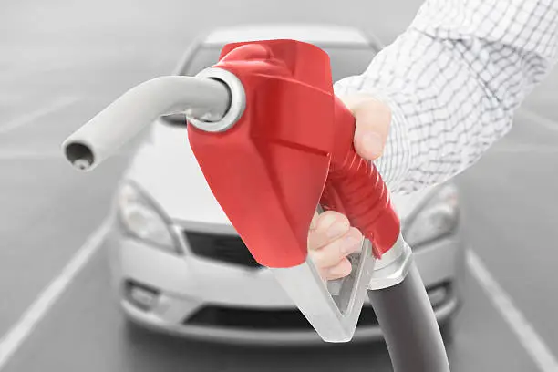 Red color fuel pump gun in hand with car on background
