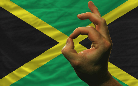 man showing excellence or ok gesture in front of complete wavy jamaica national flag of  symbolizing best quality, positivity and succes