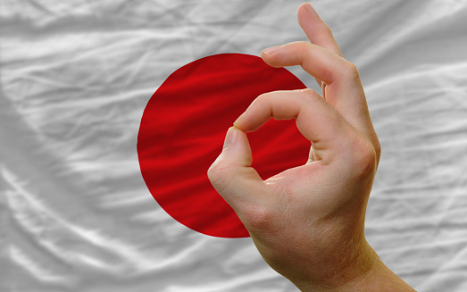 man showing excellence or ok gesture in front of complete wavy japan national flag of  symbolizing best quality, positivity and succes