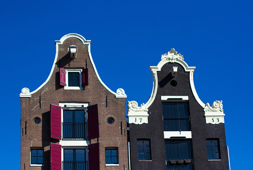 Amsterdam, Holland - August 3, 2012: Gables of two old canal-side houses--the one on the right dating from 1753--against a brilliant blue sky. 