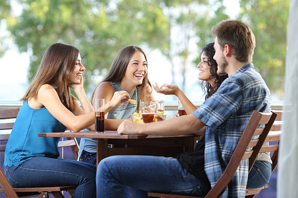 Group of friends talking and drinking at home Group of four friends talking and drinking sitting in a terrace at home family eating potato chips stock pictures, royalty-free photos & images