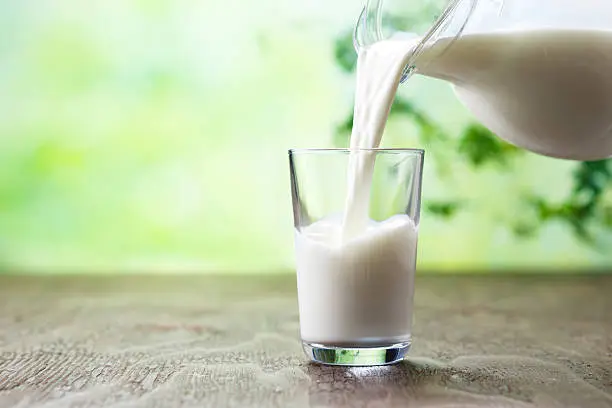 Photo of Pouring milk in the glass on the background of nature.