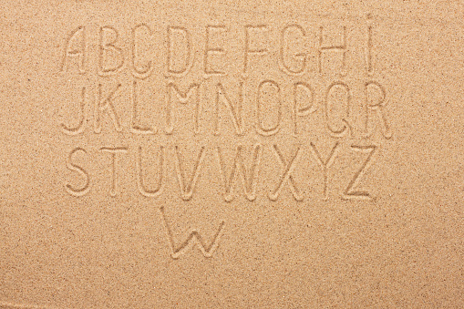 English, German, Portuguese alphabet  written on the sand, as background