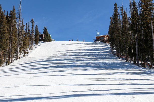 Ski run with people on top at Purgatory Skiers and snowboarders stand at the top of a large, steep ski slope at Purgatory, near Durango, Colorado.  Long shadows of pine trees stretch across the slope.  The sky is clear and blue and the ski patrol shack can be seen at the top of the hill. ski patrol photos stock pictures, royalty-free photos & images