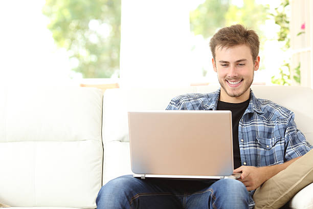 istock Man using a laptop sitting on couch at home 535495870