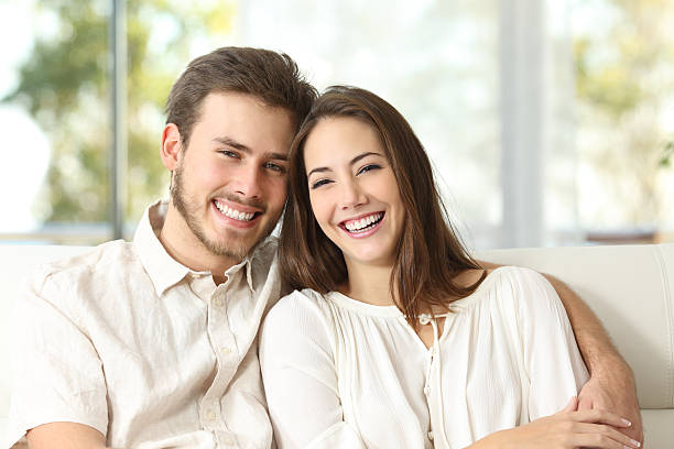 Couple at home looking at camera Happy couple sitting on a couch at home and looking at camera Marriage and Family Therapy stock pictures, royalty-free photos & images