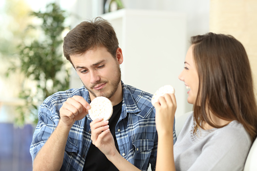 Couple enjoying and suffering diet with girlfriend offering a dietetic cookie and the boyfriend disgusted