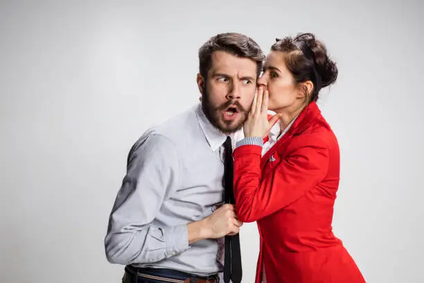 Photo of Young man telling gossips to his woman colleague at the