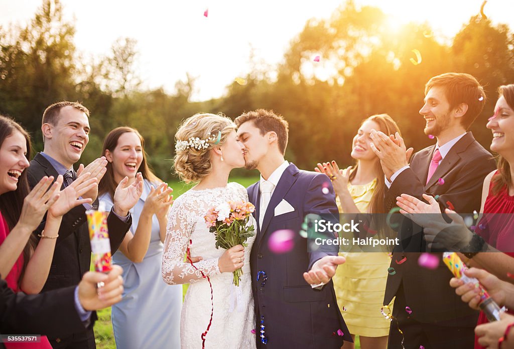 Newlyweds with guest on their garden party Full length portrait of newlywed couple and their friends at the wedding party showered with confetti in green sunny park Wedding Stock Photo